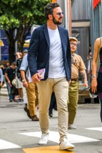 Modern man wearing a minimalist capsule wardrobe with navy blazer, white t-shirt, dark jeans and white sneakers.